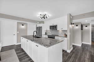 Kitchen featuring light stone counters, white cabinetry, tasteful backsplash, stainless steel appliances, and a kitchen island with sink