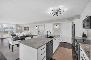 Kitchen featuring stainless steel appliances, white cabinetry, open floor plan, and light stone countertops