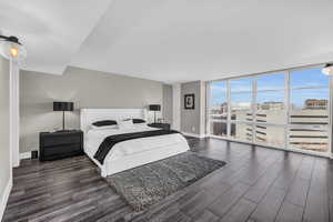 Bedroom with dark wood-type flooring, a wall of windows, and a city view