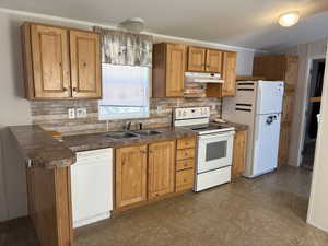 Kitchen featuring white appliances, tasteful backsplash, dark countertops, and under cabinet range hood
