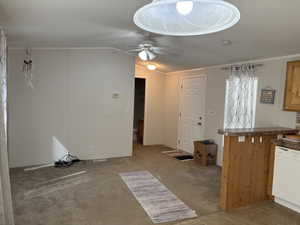 Kitchen with light colored carpet, white dishwasher, ornamental molding, vaulted ceiling, and a ceiling fan