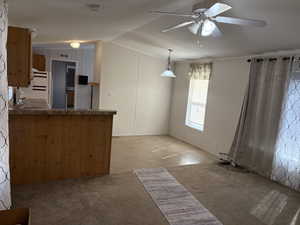 Kitchen with light colored carpet, a ceiling fan, vaulted ceiling, dark countertops, and freestanding refrigerator