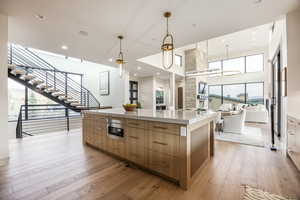 Kitchen with modern cabinets, light wood finished floors, a spacious island, hanging light fixtures, and brown cabinets