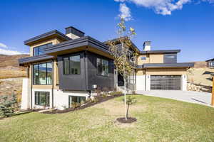 Contemporary home featuring a chimney, concrete driveway, a front lawn, and an attached garage