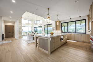 Kitchen featuring decorative light fixtures, a breakfast bar, light wood-style floors, modern cabinets, and light stone countertops