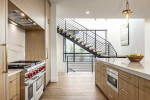 Kitchen with stainless steel appliances, modern cabinets, light stone countertops, pendant lighting, and light wood finished floors