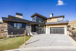 Contemporary house featuring a chimney, driveway, a garage, and a front yard