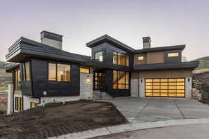 Modern home featuring driveway, a chimney, an attached garage, and stone siding