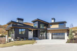 Contemporary house featuring a chimney, an attached garage, concrete driveway, and stone siding