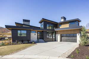 Contemporary home with a chimney, an attached garage, driveway, and stone siding