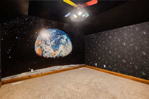 Carpeted home theater room featuring wallpapered walls, vaulted ceiling, and ceiling fan