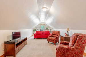 Loft with a textured ceiling, light colored carpet, and vaulted ceiling