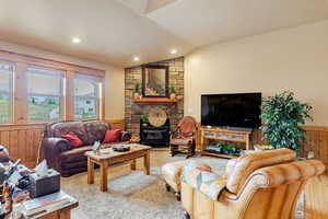 Living area featuring lofted ceiling, a fireplace, recessed lighting, a wainscoted wall, and wooden walls