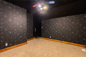 Carpeted cinema room with wallpapered walls, vaulted ceiling, and a ceiling fan