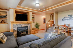 Living area with a raised ceiling, carpet flooring, ornamental molding, and a stone fireplace