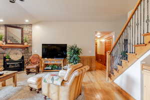 Living room with stairway, vaulted ceiling, wainscoting, wood-type flooring, and a fireplace