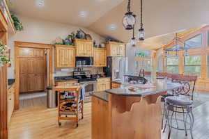 Kitchen with stainless steel appliances, light wood-style flooring, hanging light fixtures, light brown cabinets, and a kitchen breakfast bar