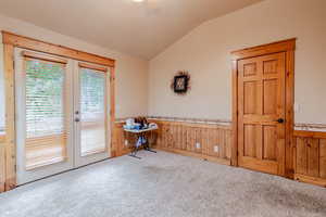 Carpeted empty room featuring lofted ceiling, wood walls, french doors, and wainscoting