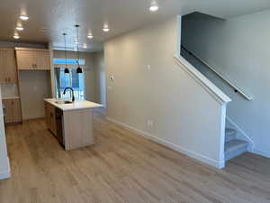 Kitchen featuring a textured ceiling, an island with sink, decorative light fixtures, light wood-type flooring, and light brown cabinetry