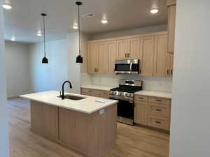 Kitchen featuring stainless steel appliances, decorative backsplash, an island with sink, light wood finished floors, and a textured ceiling