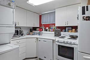 Kitchen with white appliances, white cabinets, light countertops, and estacked washer and dryer