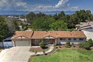 Single story home featuring a mountain view, concrete driveway, an attached garage, a chimney, and stone siding