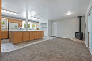 Kitchen featuring light tile patterned floors, light carpet, a textured ceiling, light countertops, and a wood stove