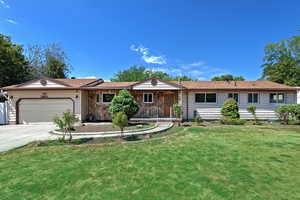 Ranch-style home with driveway, a front yard, stone siding, an attached garage, and covered porch