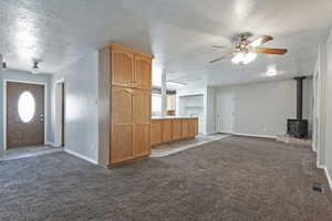 Unfurnished living room with a textured ceiling, a wood stove, carpet flooring, and ceiling fan