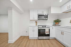 Kitchen with stainless steel appliances, white cabinets, light wood-style floors, and recessed lighting