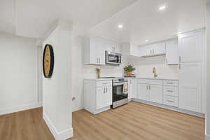 Kitchen featuring light countertops, white cabinetry, stainless steel appliances, light wood finished floors, and recessed lighting