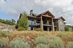 Back of house featuring a metal roof, a standing seam roof, stone siding, a chimney, and a balcony