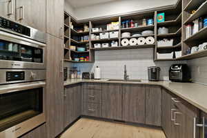 Kitchen with stainless steel double oven, modern cabinets, light wood-type flooring, and tasteful backsplash