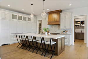 Kitchen featuring a breakfast bar area, an island with sink, decorative backsplash, white cabinetry, and light wood-style flooring