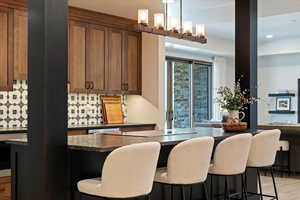 Kitchen featuring dark countertops, a kitchen bar, hanging light fixtures, decorative backsplash, and wood finished floors