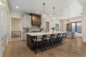 Kitchen with decorative backsplash, a breakfast bar, hanging light fixtures, a center island with sink, and light wood-style floors