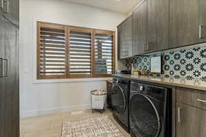 Washroom featuring light tile patterned flooring, cabinet space, and washing machine and clothes dryer