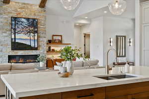 Kitchen with open floor plan, light stone countertops, a stone fireplace, brown cabinets, and decorative light fixtures