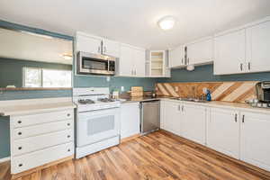 Kitchen with appliances with stainless steel finishes, white cabinets, light countertops, and light wood-style floors