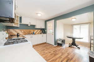 Kitchen featuring light countertops, backsplash, light wood-style flooring, white cabinetry, and stainless steel microwave