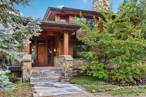 Entrance to property featuring a porch, a chimney, and stone siding