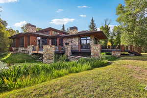 Rear view of property featuring a chimney, a yard, a wooden deck, and stone siding