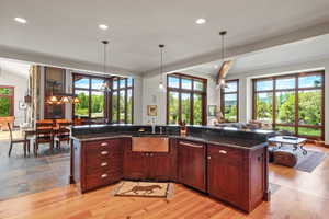 Kitchen featuring a center island with sink, recessed lighting, hanging light fixtures, dark stone counters, and light wood finished floors