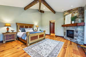 Bedroom with beamed ceiling, light wood-style floors, a stone fireplace, and high vaulted ceiling