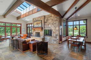 Living area with beamed ceiling, plenty of natural light, a fireplace, stone tile flooring, and high vaulted ceiling