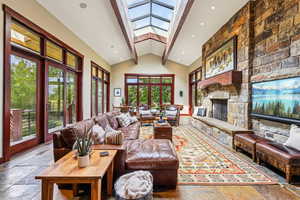 Living room featuring a skylight, beamed ceiling, a stone fireplace, stone tile flooring, and high vaulted ceiling