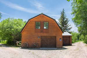 View of side of home with a gambrel roof, a barn, and an outbuilding