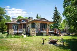 Back of property with a chimney, a wooden deck, an outdoor fire pit, a yard, and stone siding