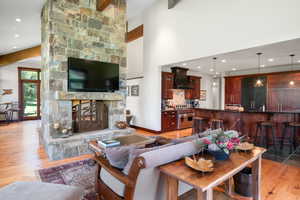 Living area with beamed ceiling, light wood finished floors, recessed lighting, bar with sink, and a stone fireplace