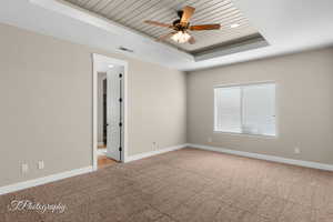 Unfurnished room featuring a raised ceiling, light carpet, wood ceiling, and a ceiling fan